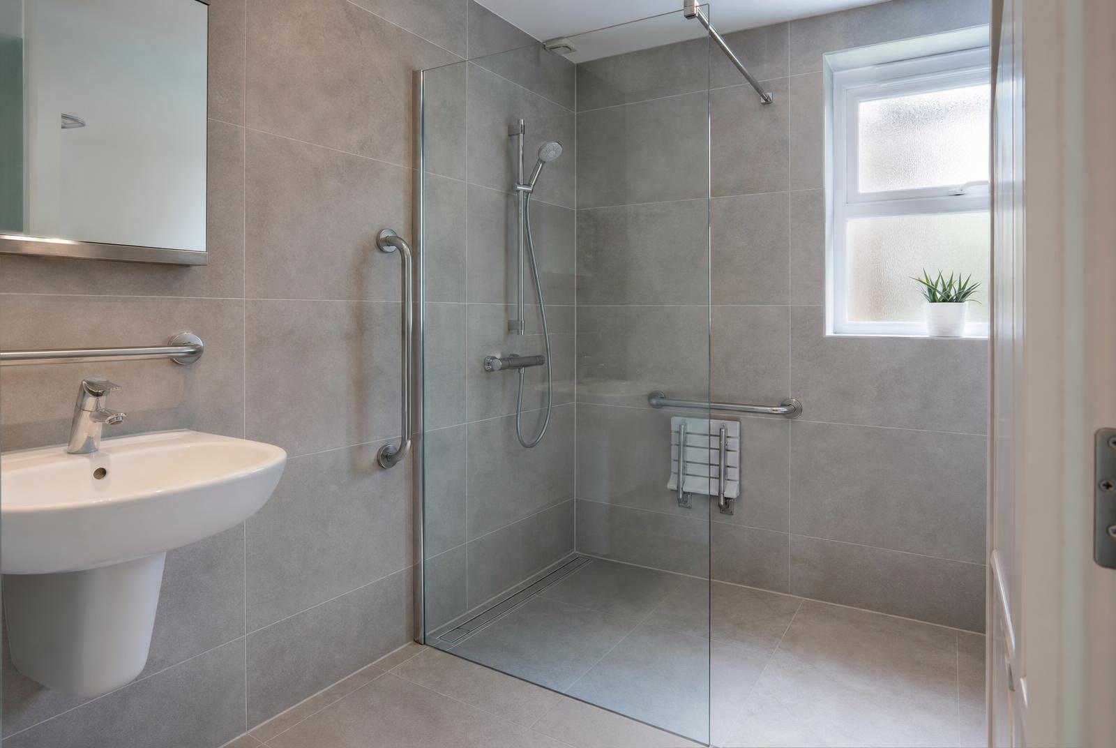 Level-access wet room with grey tiling, linear drain, grab rails and a folding shower seat